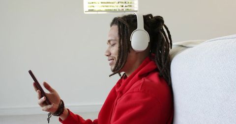 African american man relaxing with headphones and smartphone on couch wearing red hoodie