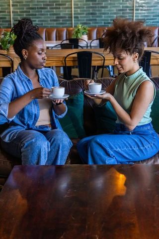 Diverse friends sipping coffee and sharing conversation on leather sofa in cozy cafe