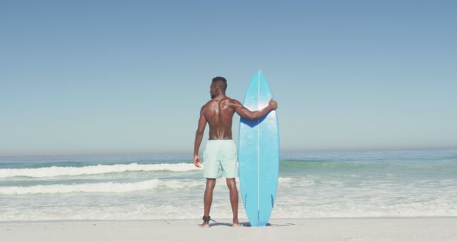 Back view african american man standing on beach with surfboard and looking on sea. Summer, relaxation, vacation, happy time, summer time.