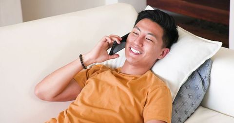 Smiling Young Man Pleasantly Talking on Smartphone at Home