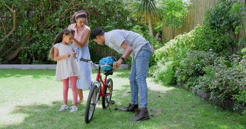 Father Adjusting Daughter's Bicycle While Family Enjoys Sunny Day
