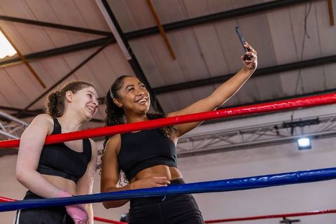 Young female boxers posing for selfie in boxing ring after training, smiling teammates