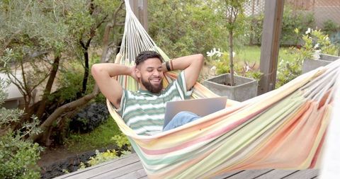 Man relaxing in garden hammock with laptop enjoying leisure time outdoors