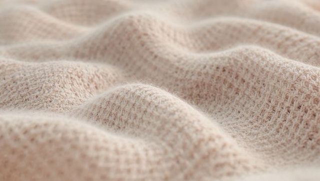 Waffle-knit textile close-up showing soft beige-peach yarn fuzz and cozy woven texture