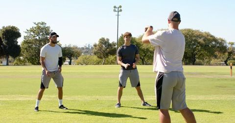 Diverse male athletes training on sunny field practicing throwing and catching drills