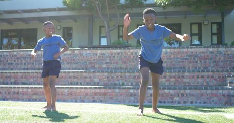 African american teens running barefoot on sunlit lawn by brick steps, laughing