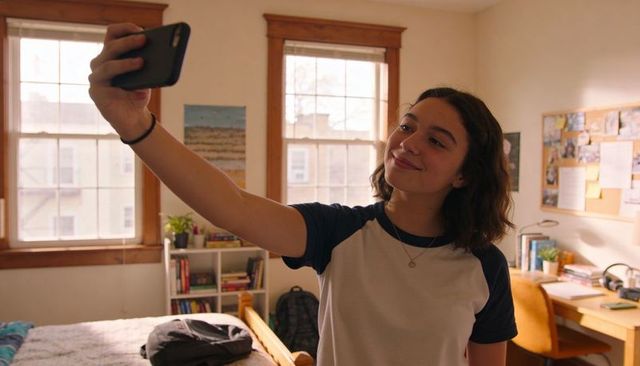 Teen student taking selfie in sunlit dorm room with cozy desk, books, backpack