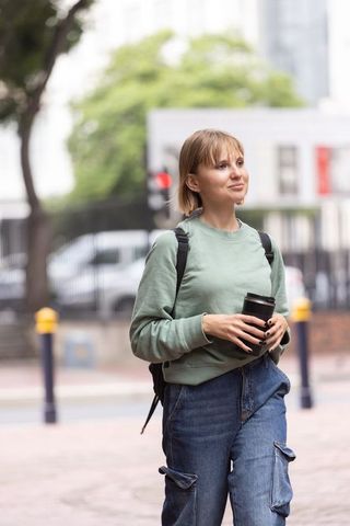 Young woman walking with reusable tumbler in cargo jeans and green sweatshirt