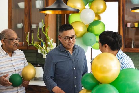 Diverse seniors decorating kitchen with green and gold balloons celebrating family reunion
