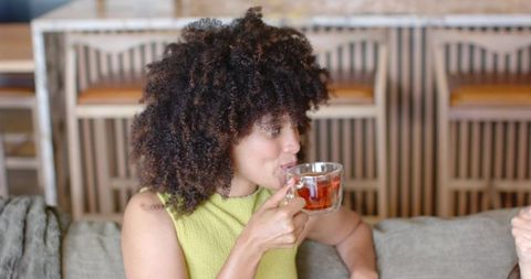 African american woman sipping tea on sofa in cozy cafe with double-wall glass cup