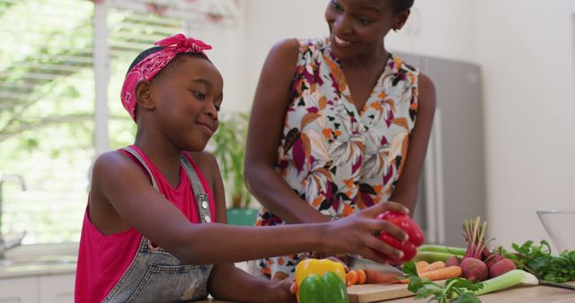 African American mother and daughter spending quality time cooking together in kitchen, preparing colorful vegetables. Perfect for advertisements promoting family bonding, healthy eating, culinary experiences, and multicultural family lifestyles.