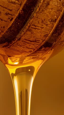Vertical macro of golden viscous liquid dripping, textured surface and luxury abstract motion