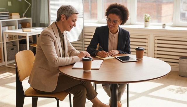 Businesswomen discussing plan and taking notes at round table in sunlit office