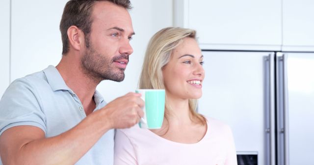 A Caucasian man and woman, both appearing to be middle-aged, share a moment in a kitchen setting, with copy space. They seem relaxed and comfortable, enjoying a casual conversation over a cup of coffee or tea.
