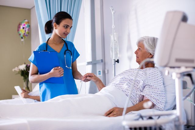 Female doctor holding elderly patient's hand in hospital ward. The scene shows a medical professional providing compassionate care and conducting a health check. The patient is lying in a hospital bed with medical equipment nearby. This image can be used in healthcare promotions, medical services advertising, patient care guides, and hospital brochures.