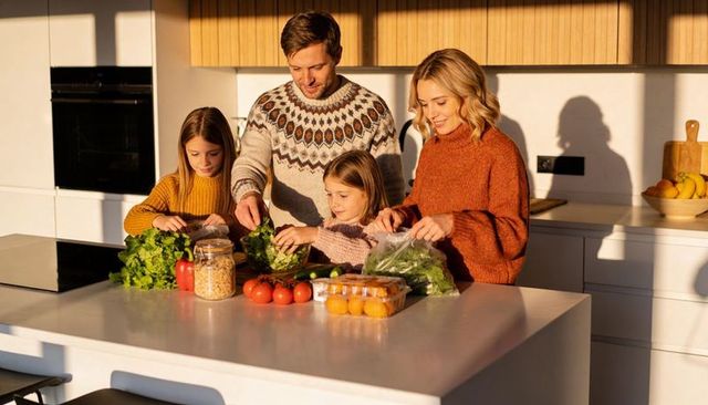 Sunlit family preparing fresh salad and eggs on white modern kitchen island cooking together