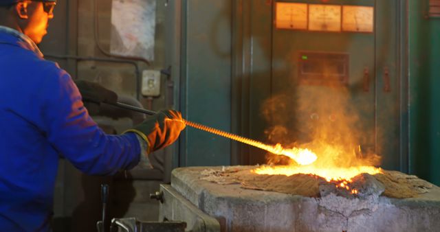 This image depicts an industrial worker melting metal in a furnace. The worker, wearing protective gloves and a safety suit, is manipulating a rod to adjust the melting process. Strong visualization of heavy industry and labor-intensive work. Perfect for illustrating themes of metallurgy, manufacturing, heat work, labor safety, and industrial processes. Useful for articles, websites, or marketing materials focused on industrial work, safety in manufacturing, or blue-collar professions.