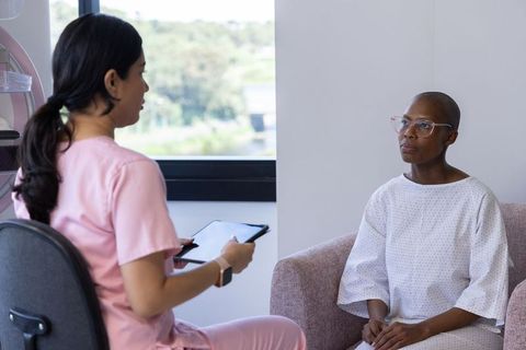 African American patient consulting clinician as nurse in pink scrubs holds tablet