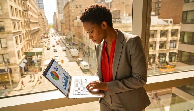 Executive analyzing business charts on laptop by office window overlooking city street