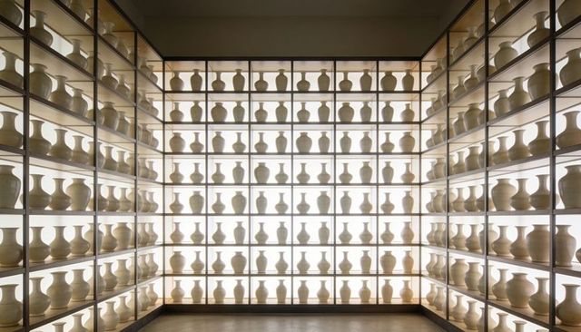 Backlit gallery wall displaying symmetrical cream ceramic vases on illuminated shelves