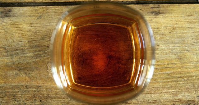 A glass of amber-colored liquid, whiskey or tea, sits atop a rustic wooden surface, with copy space. Its warm hue invites a sense of relaxation or a moment of pause in a cozy setting.