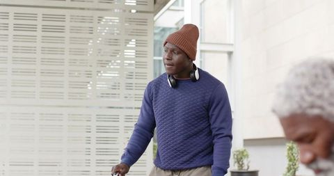 African American commuter standing with scooter holding handle wearing beanie headphones