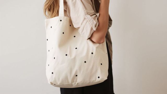Carrying cream canvas tote bag with black polka dots, minimalist fashion accessory