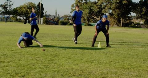 Male athletes practicing field drills on sunny park grass with red ball and yellow cone