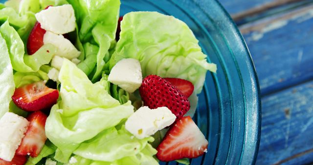 Fresh and vibrant salad featuring lettuce, strawberries, and feta cheese in blue bowl. Perfect for healthy eating, vegetarian meals, diet blogs, recipe websites, or dietary plans that promote fresh and nutritious food choices.