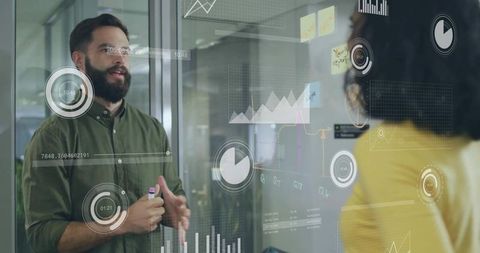 Male presenting data visualizations on glass wall during team collaboration in office