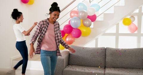 Cheerful women decorating living room with balloons for celebration