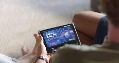 Man holding tablet watching retro neon car poster 'Into the Knight' while relaxing on rug