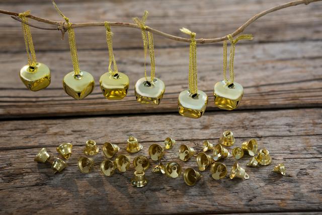 Golden Christmas bells hanging on a twig above a rustic wooden surface. This festive scene can be used for holiday greeting cards, Christmas invitations, and seasonal decor ideas. The rustic background adds a warm and vintage feel perfect for winter celebrations and holiday promotions.