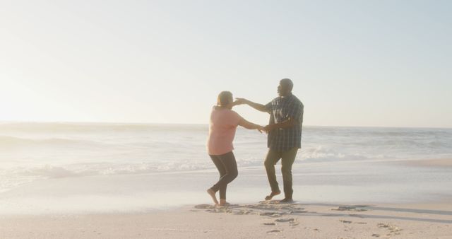 Smiling senior african american couple holding hands and dancing on sunny beach - Download Free Stock Photos Pikwizard.com