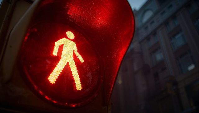 Glowing red pedestrian signal at city intersection showing walking figure under visor