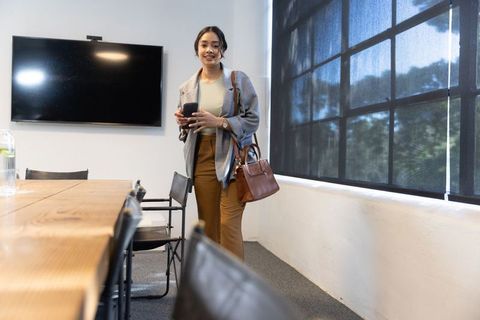 Confident Hispanic Businesswoman Checking Smartphone in Modern Conference Room
