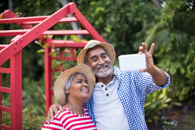 Senior couple enjoying a sunny day in their garden, capturing a happy moment with a selfie. Ideal for use in advertisements promoting senior lifestyle, retirement communities, outdoor activities, and family bonding. Perfect for illustrating themes of happiness, togetherness, and active aging.