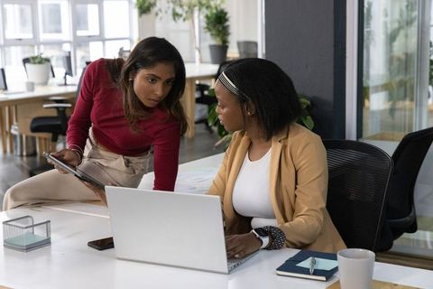 Diverse coworkers collaborating at laptop and tablet in bright modern office workspace