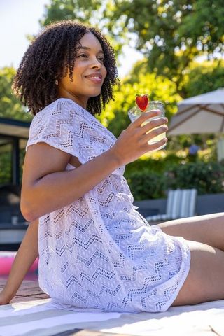 African american woman relaxing poolside in white knit coverup holding strawberry drink