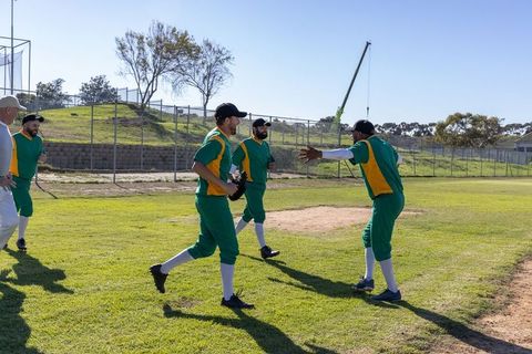 Baseball players regrouping and celebrating after out call walking on sunny grass field