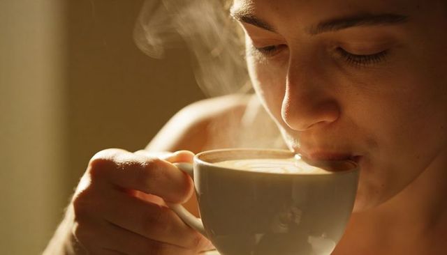 Sipping morning latte closeup, woman enjoying steaming ceramic cup, cozy warm soft glow