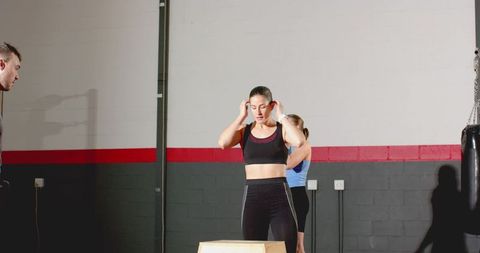 Woman adjusting earbuds before box jump during group training in gym with punching bag