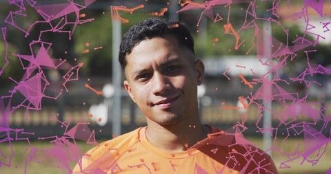 Young male athlete smiling on sunny football pitch in orange jersey with purple geometric overlay