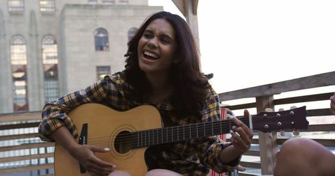 Joyful Woman Playing Guitar and Singing on City Rooftop