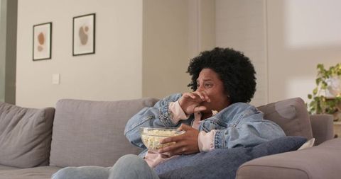 African american woman watching movie on couch eating popcorn during cozy home evening