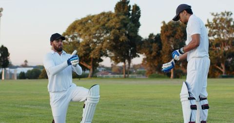 Cricket teammates preparing for batting during golden hour, adjusting gloves and leg pads