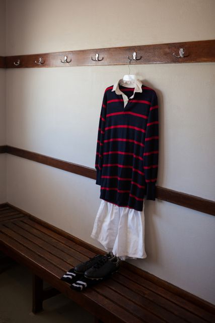 Rugby uniform hanging neatly on wooden bench in locker room, with shoes and socks placed below. Ideal for use in sports-related content, team preparation visuals, or athletic apparel promotions.