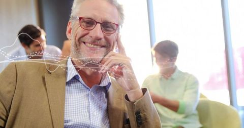 Smiling senior executive relaxing in modern office lounge wearing red glasses tan blazer