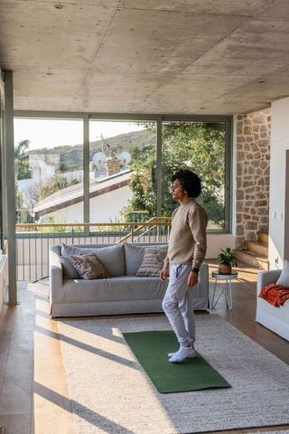 Young black man practicing mindful stretching on yoga mat in bright modern living room
