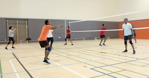 Diverse male volleyball players playing indoors in school gym, man receiving near net